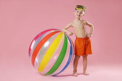 Photo of Cute little boy in beachwear with diving mask and inflatable ball on pink background