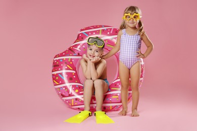 Photo of Cute little kids in beachwear with inflatable ring on pink background