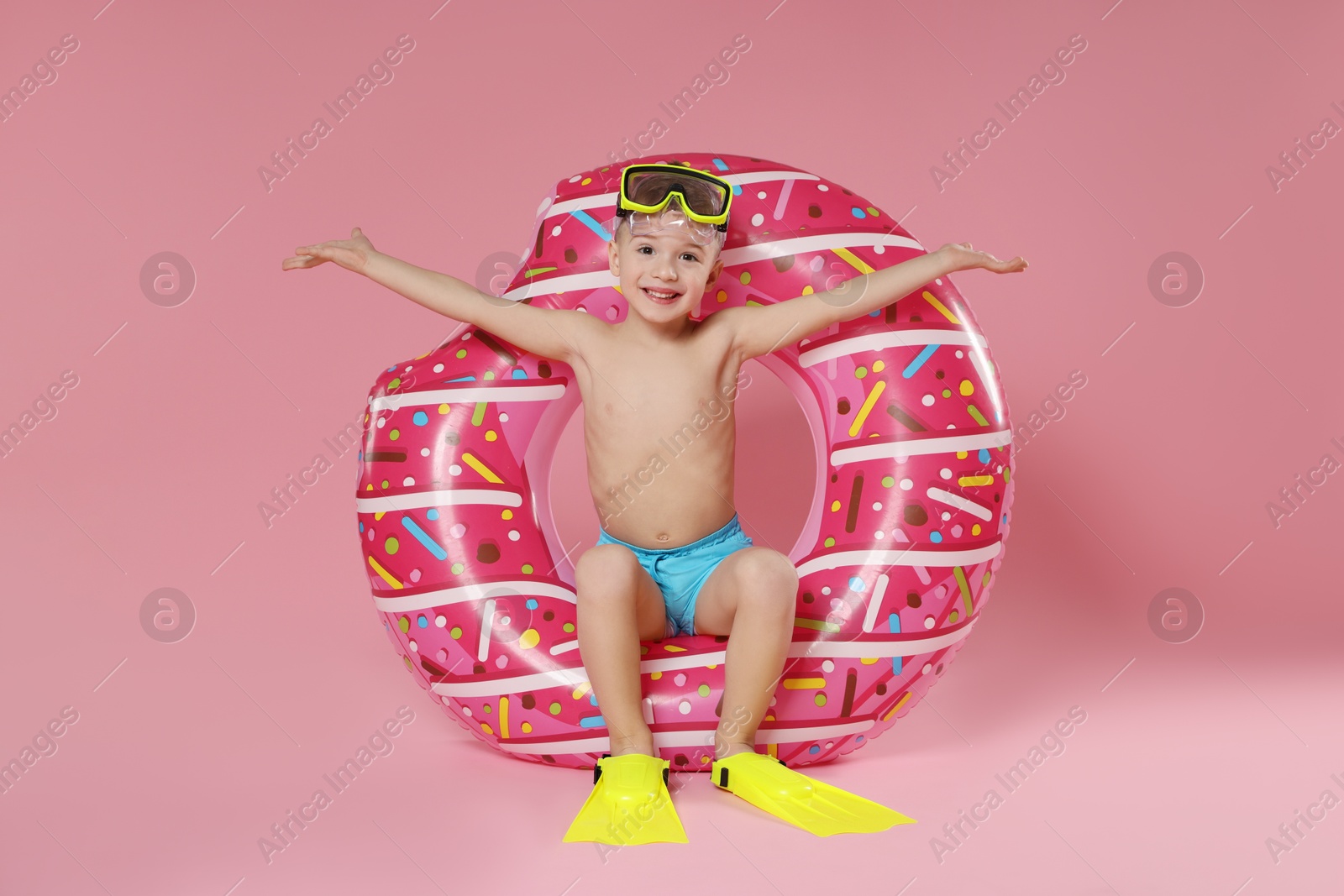 Photo of Cute little boy in beachwear with diving mask, flippers and inflatable ring on pink background