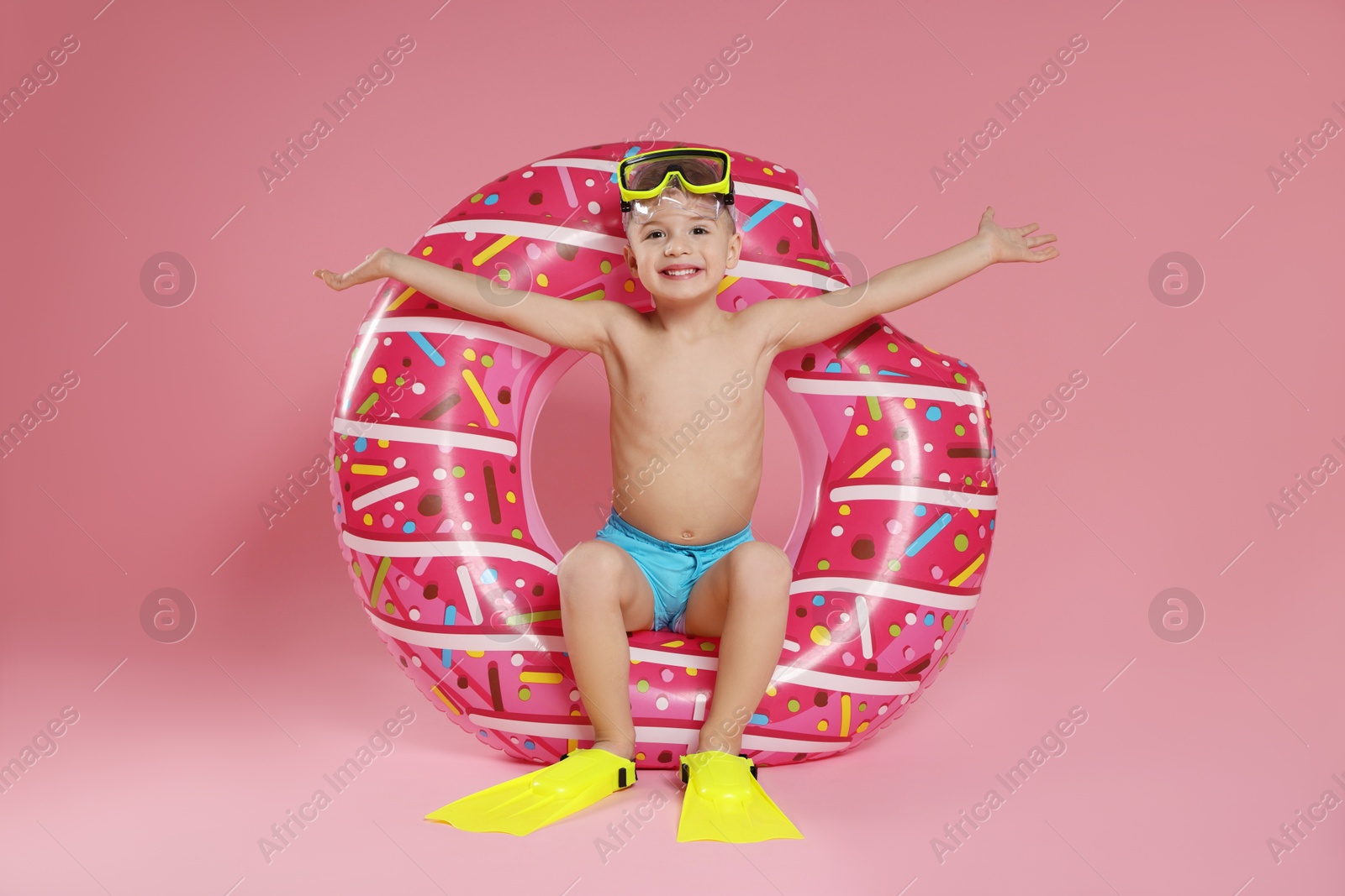 Photo of Cute little boy in beachwear with diving mask, flippers and inflatable ring on pink background