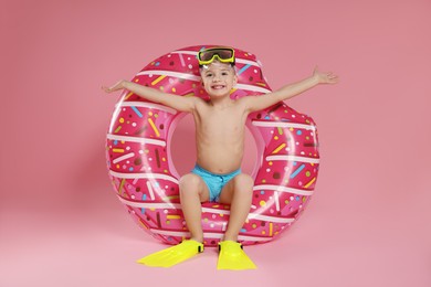 Photo of Cute little boy in beachwear with diving mask, flippers and inflatable ring on pink background