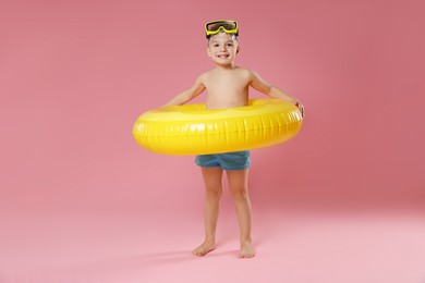 Cute little boy in beachwear with diving mask and inflatable ring on pink background