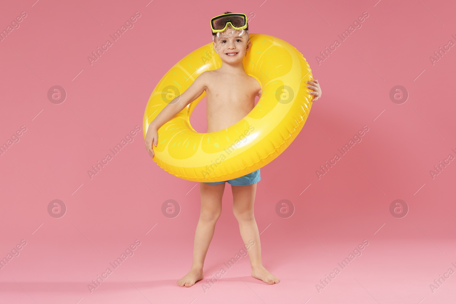 Photo of Cute little boy in beachwear with diving mask and inflatable ring on pink background