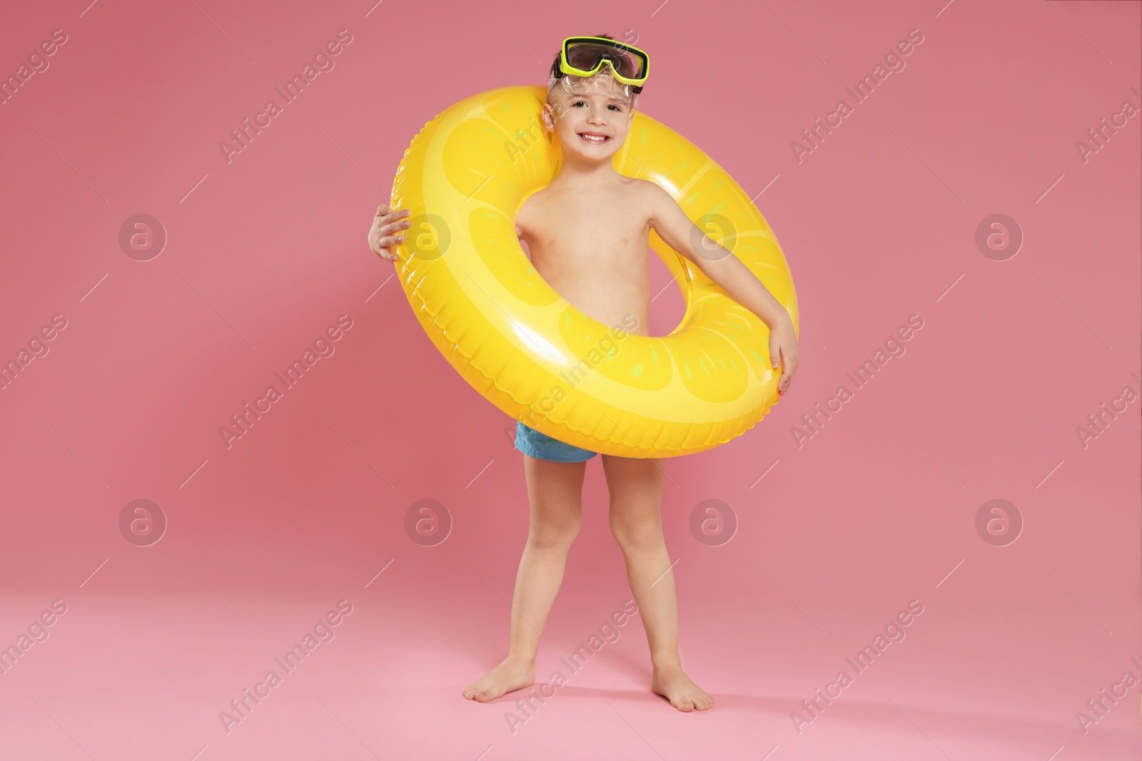 Photo of Cute little boy in beachwear with diving mask and inflatable ring on pink background