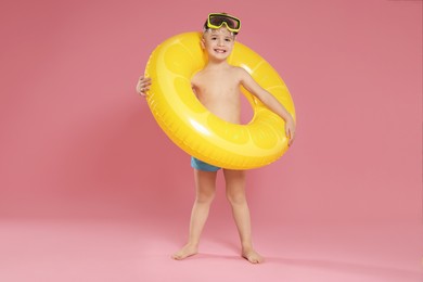 Cute little boy in beachwear with diving mask and inflatable ring on pink background