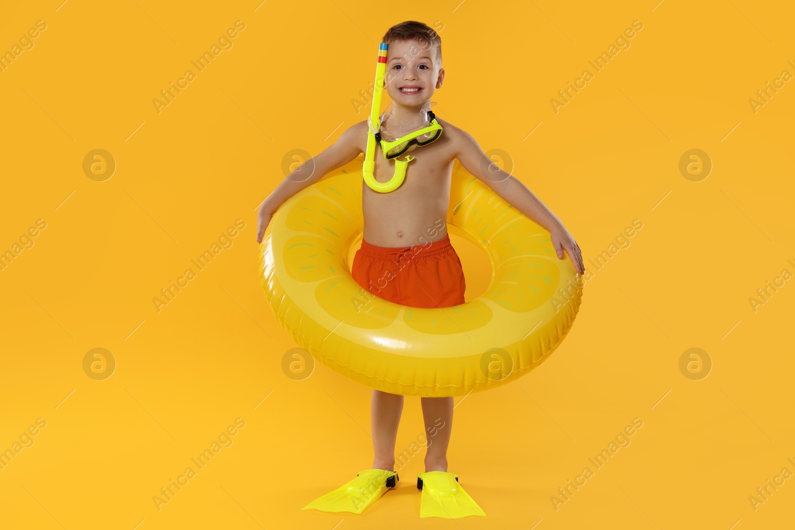 Photo of Cute little boy in beachwear with snorkeling equipment and inflatable ring on orange background