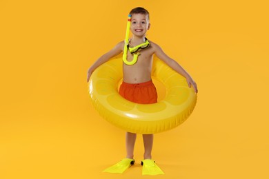 Photo of Cute little boy in beachwear with snorkeling equipment and inflatable ring on orange background