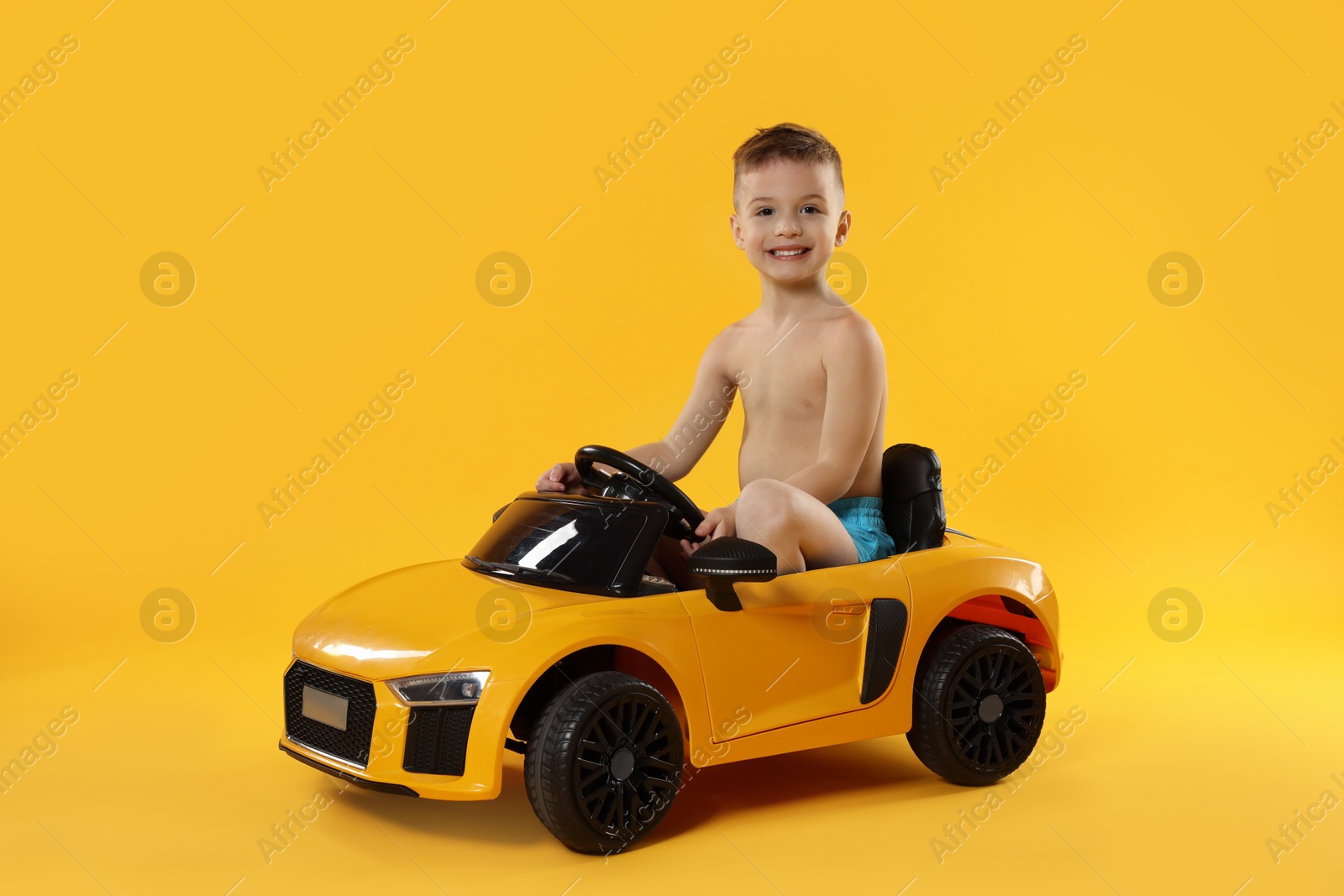 Photo of Cute little boy in beachwear with toy car on orange background