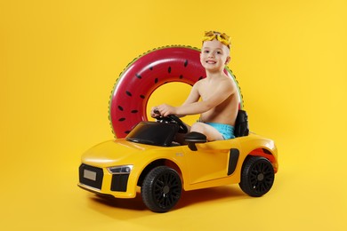 Cute little boy in beachwear with inflatable ring and toy car on orange background