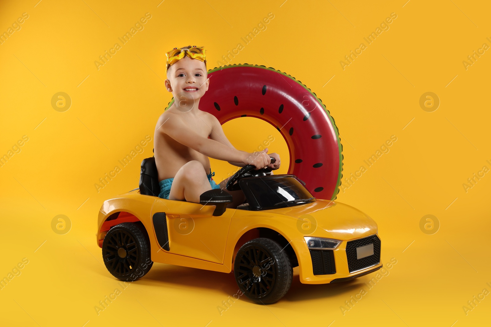 Photo of Cute little boy in beachwear with inflatable ring and toy car on orange background