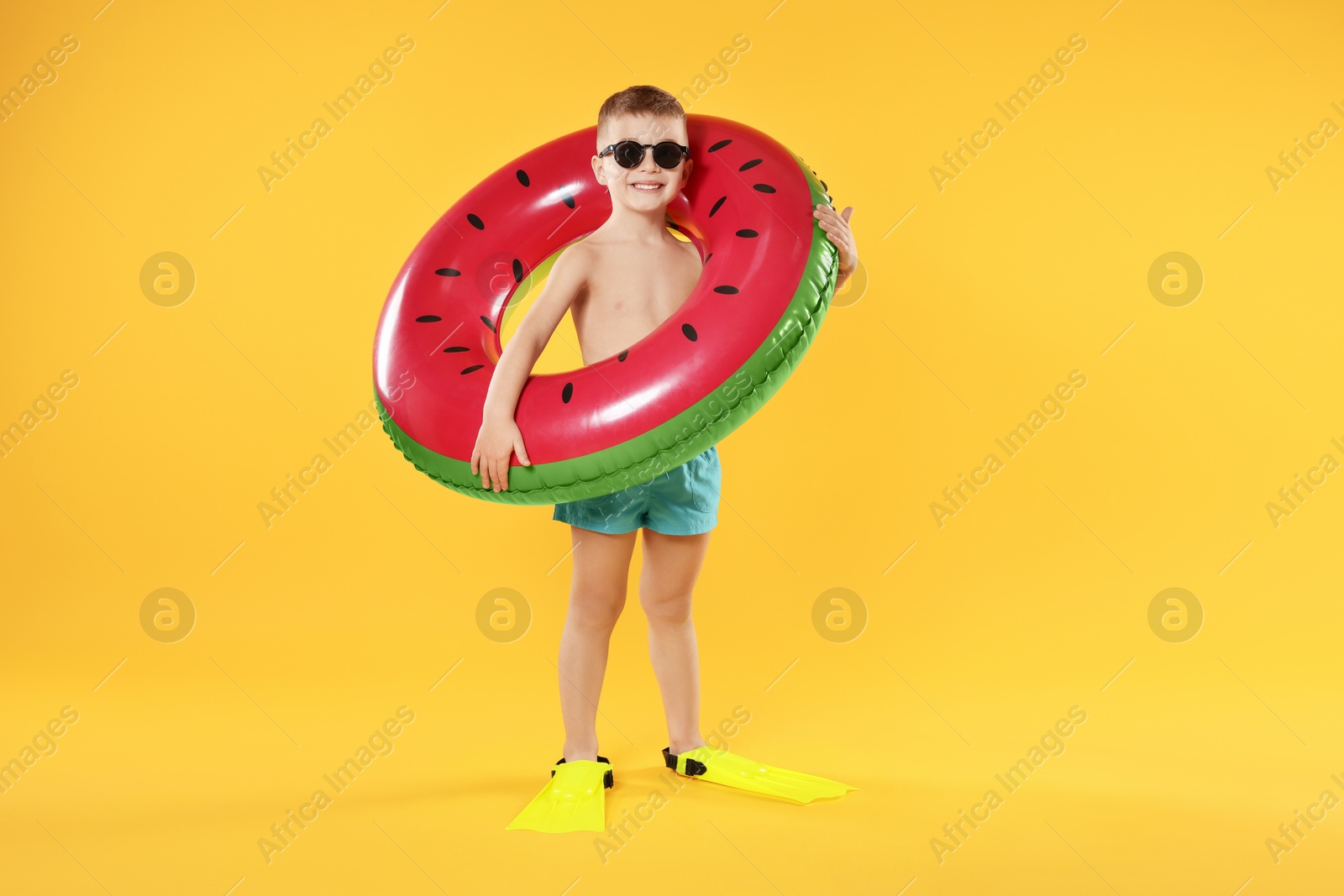 Photo of Cute little boy in beachwear with flippers and inflatable ring on orange background