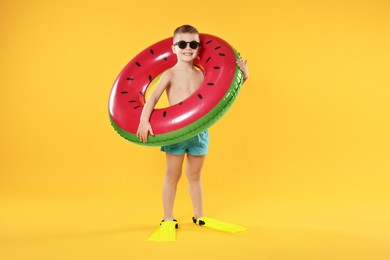 Photo of Cute little boy in beachwear with flippers and inflatable ring on orange background