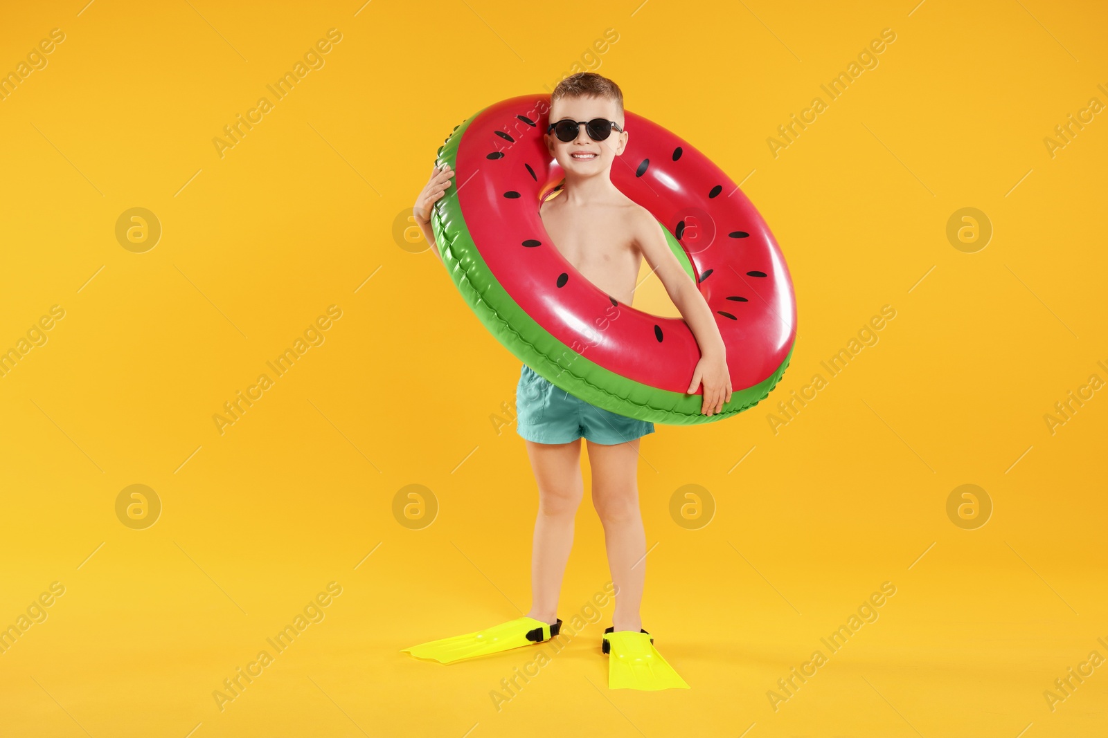 Photo of Cute little boy in beachwear with flippers and inflatable ring on orange background