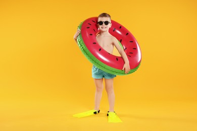 Cute little boy in beachwear with flippers and inflatable ring on orange background