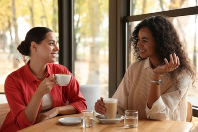 Photo of Happy women with coffee drinks chatting in cafe