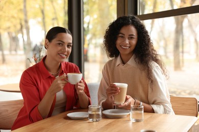 Photo of Happy women with coffee drinks at table in cafe