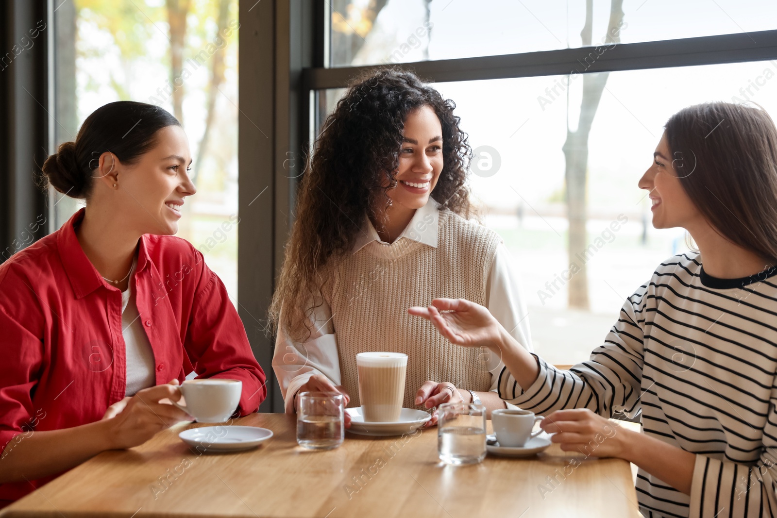 Photo of Happy women with coffee drinks chatting in cafe