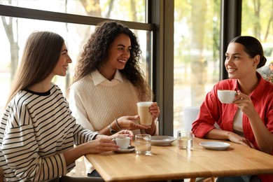 Photo of Happy women with coffee drinks chatting in cafe