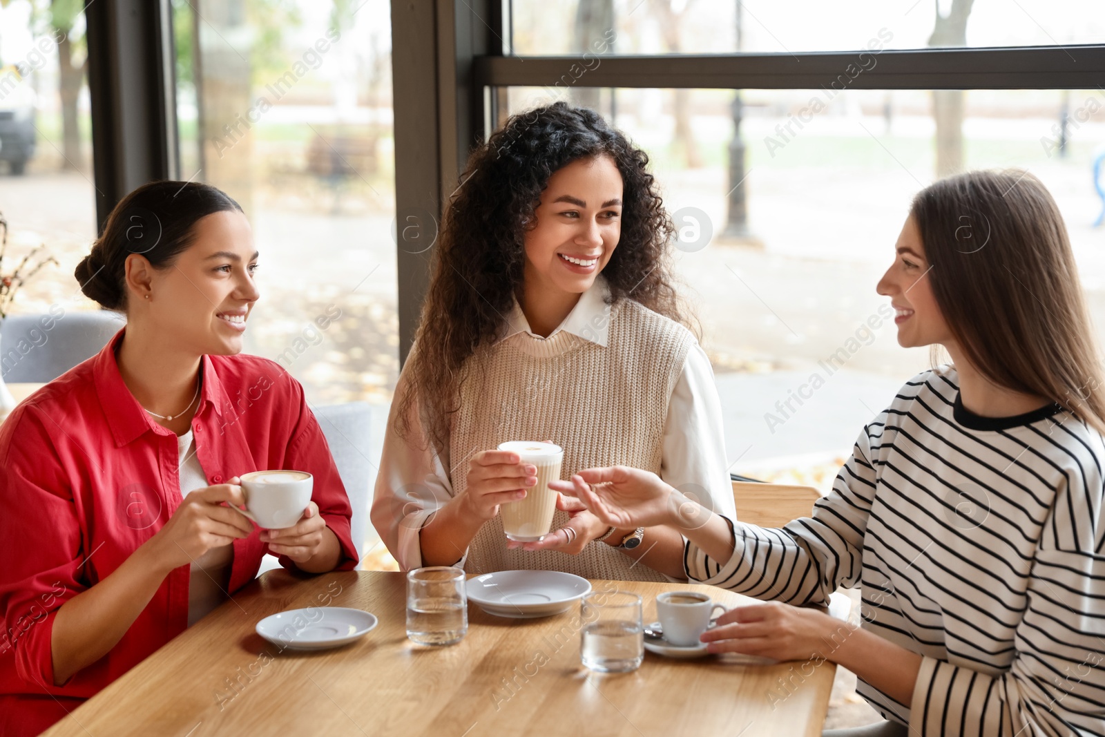 Photo of Happy women with coffee drinks chatting in cafe