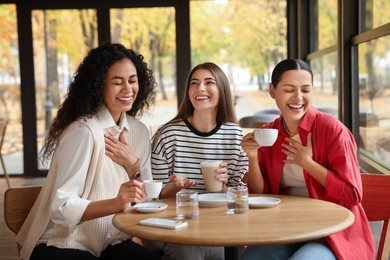 Photo of Happy women with coffee drinks at table in cafe