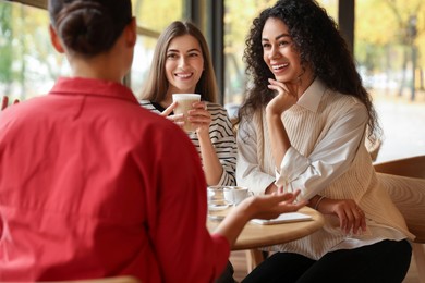 Photo of Happy women with coffee drinks chatting in cafe