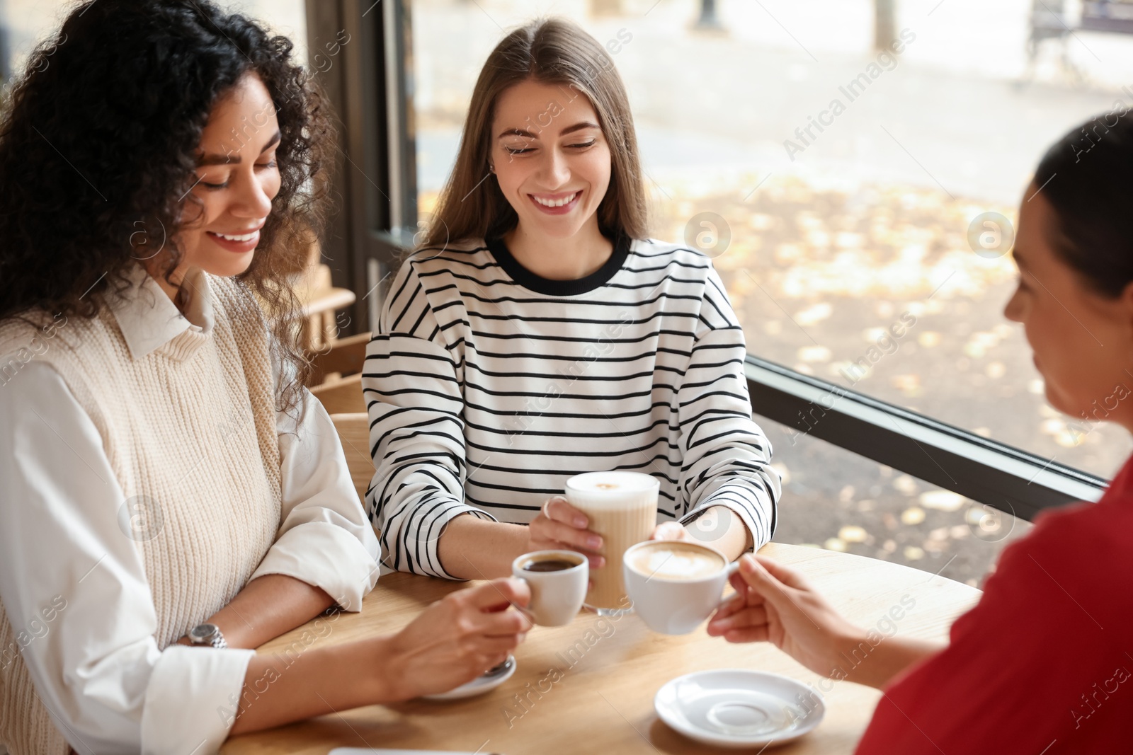 Photo of Happy women with coffee drinks chatting in cafe