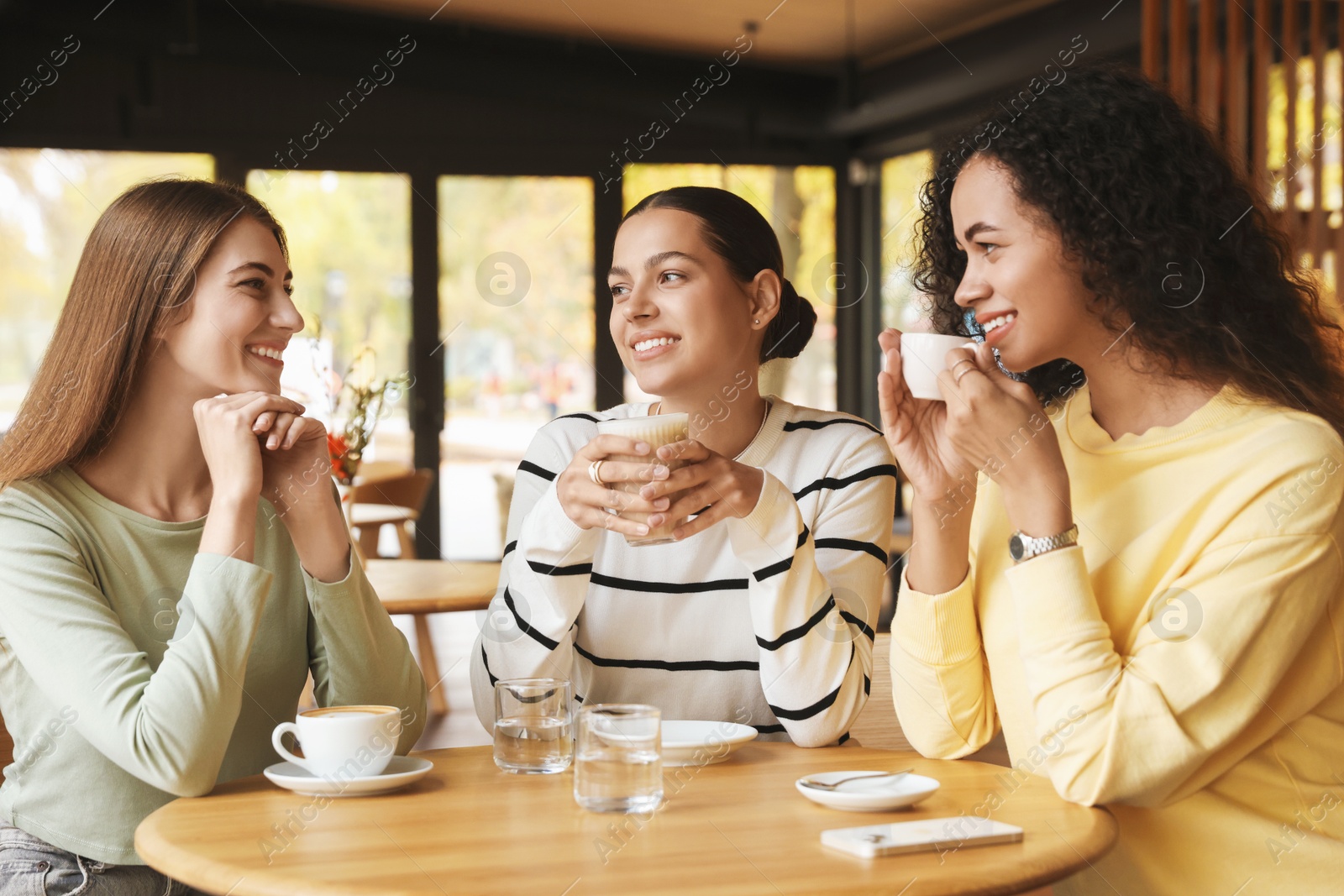 Photo of Happy women with coffee drinks chatting in cafe