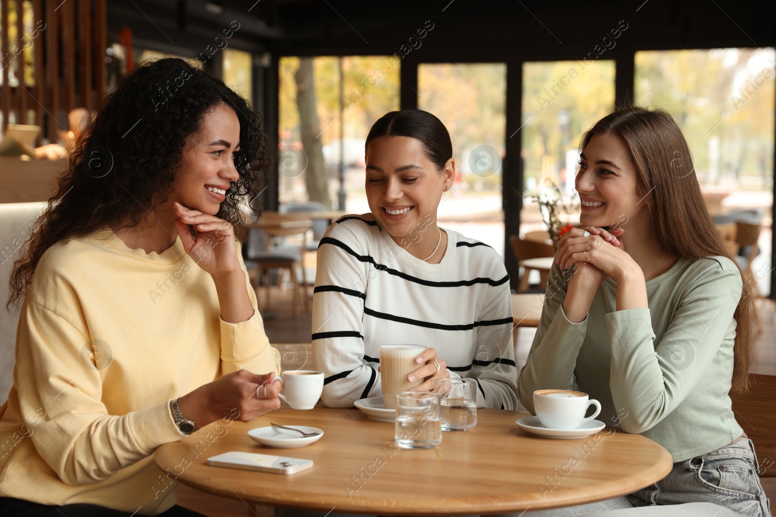 Photo of Happy women with coffee drinks chatting in cafe