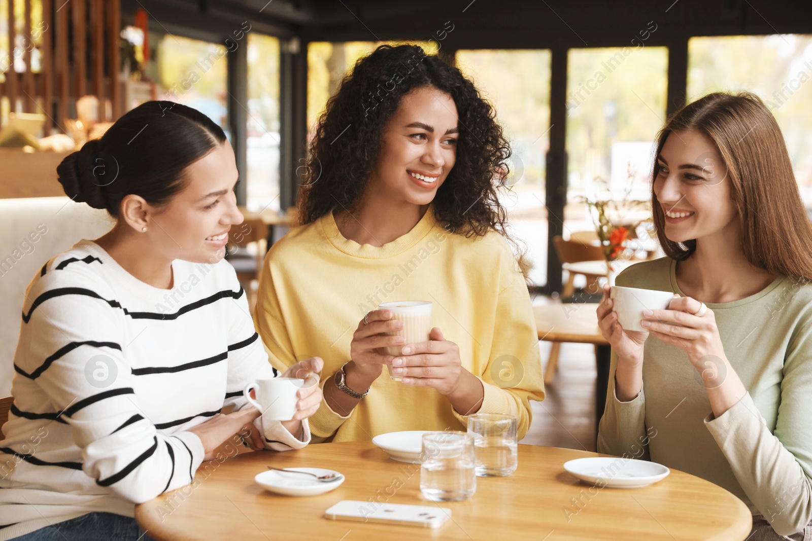 Photo of Happy women with coffee drinks chatting in cafe