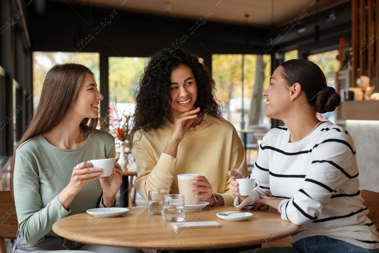 Photo of Happy women with coffee drinks chatting in cafe