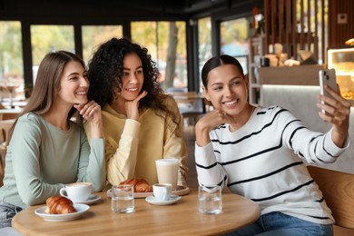 Photo of Happy friends taking selfie during coffee meeting in cafe