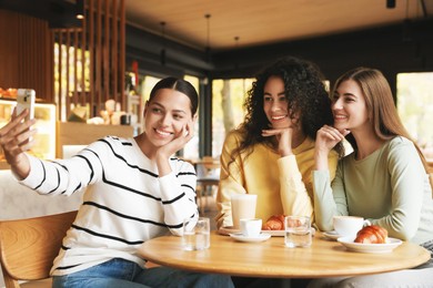 Photo of Happy friends taking selfie during coffee meeting in cafe