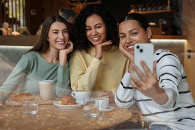 Photo of Women taking selfie at coffee meeting in cafe, view through window