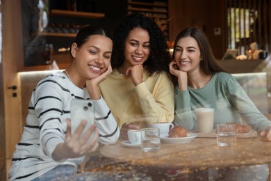 Photo of Women taking selfie at coffee meeting in cafe, view through window