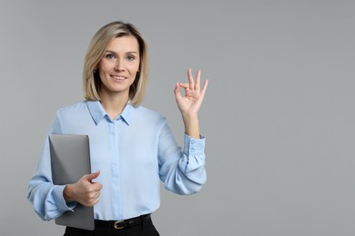 Photo of Smiling businesswoman with laptop showing okay gesture on grey background. Space for text