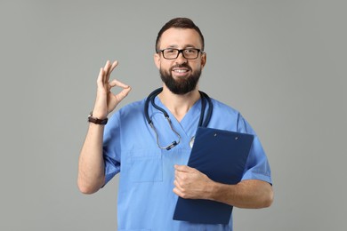 Photo of Doctor with clipboard showing okay gesture on grey background