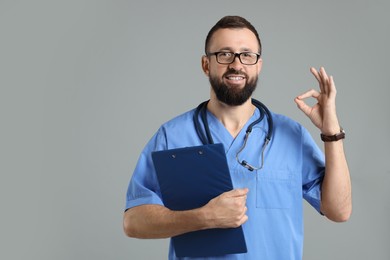 Photo of Doctor with clipboard showing okay gesture on grey background. Space for text