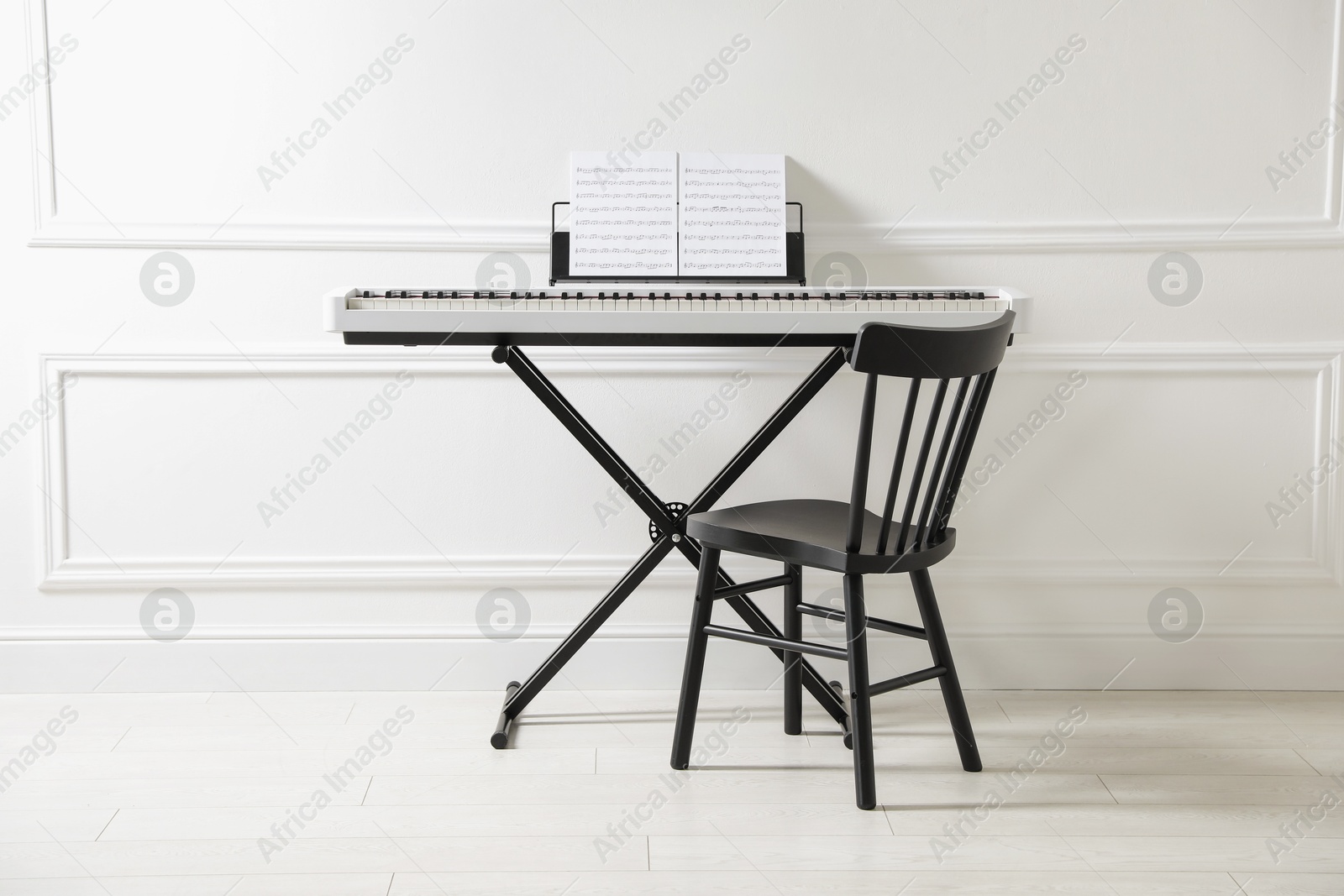 Photo of Synthesizer with music sheets and chair near white wall indoors