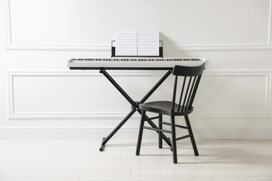 Photo of Synthesizer with music sheets and chair near white wall indoors