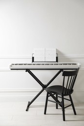 Photo of Synthesizer with music sheets and chair near white wall indoors