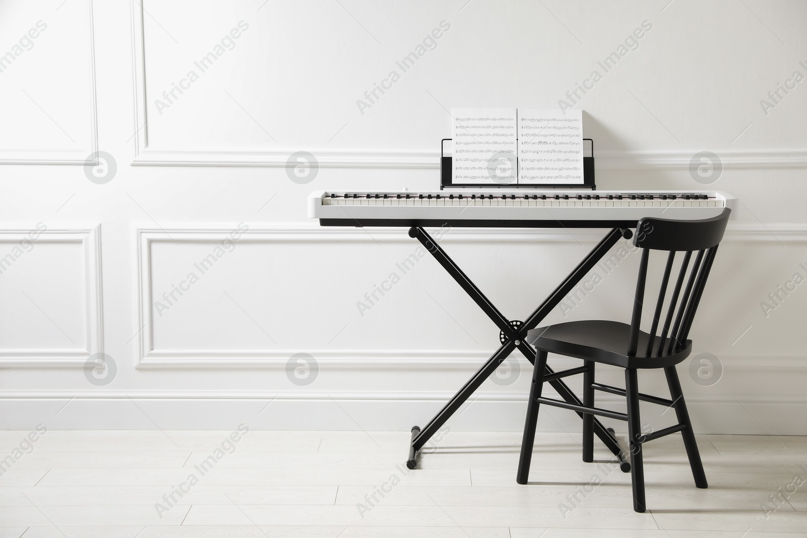 Photo of Synthesizer with music sheets and chair near white wall indoors, space for text