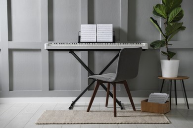 Photo of Synthesizer with music sheets and chair near grey wall indoors