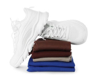 Photo of Stylish sneakers on stack of folded sportswear isolated on white