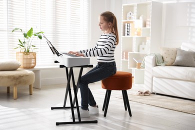 Photo of Cute girl playing synthesizer at home. Electronic musical instrument