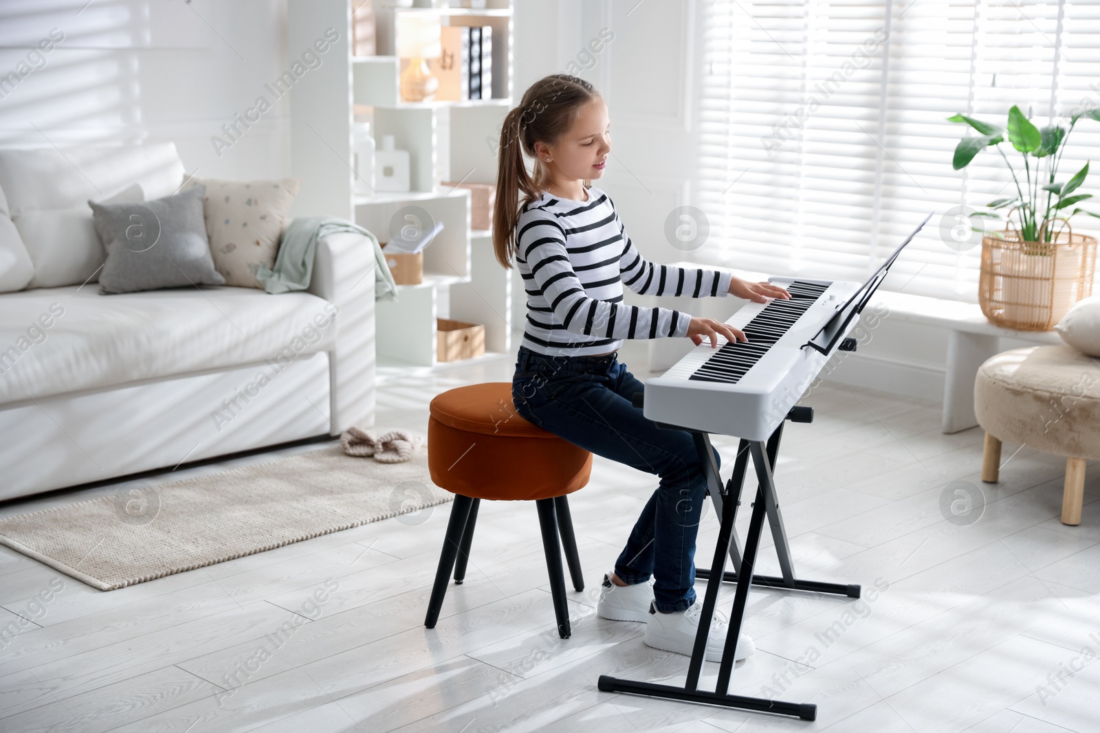 Photo of Cute girl playing synthesizer at home. Electronic musical instrument