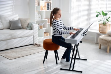 Photo of Cute girl playing synthesizer at home. Electronic musical instrument