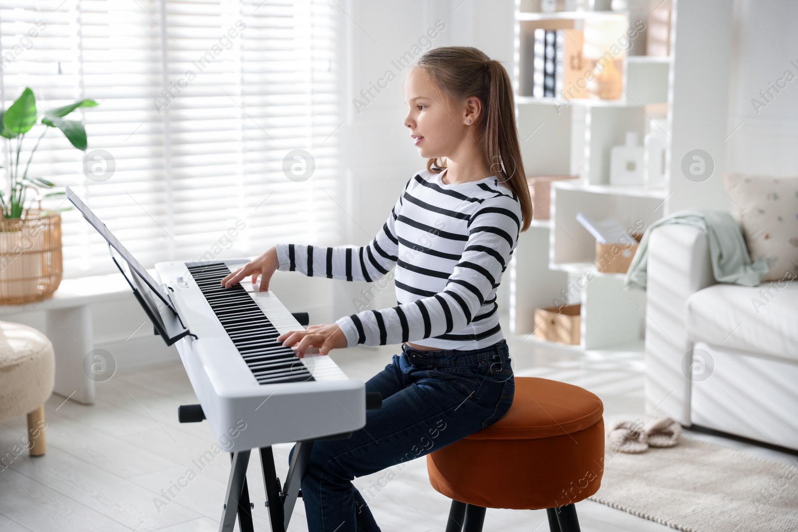 Photo of Cute girl playing synthesizer at home. Electronic musical instrument