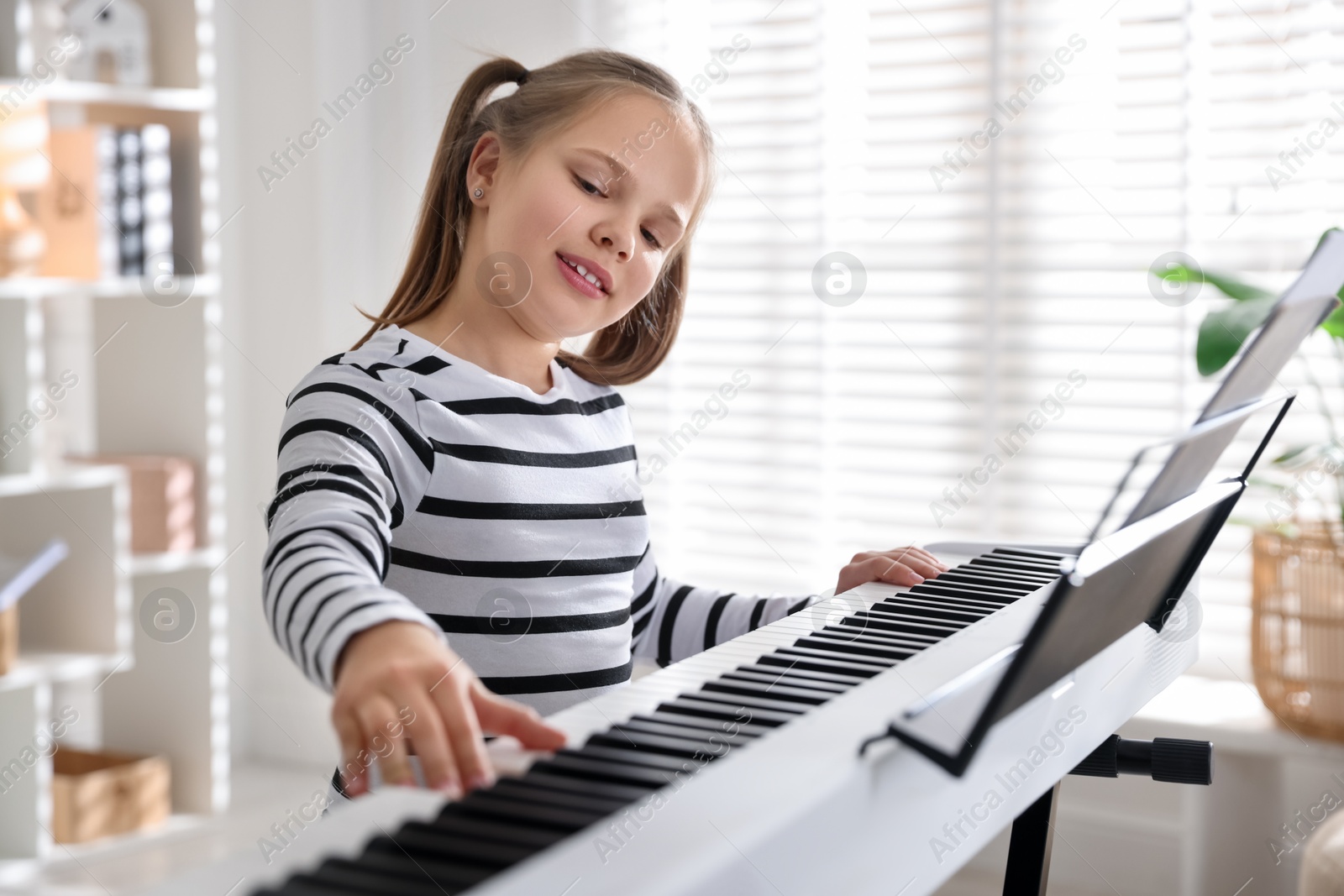 Photo of Cute girl playing synthesizer at home. Electronic musical instrument