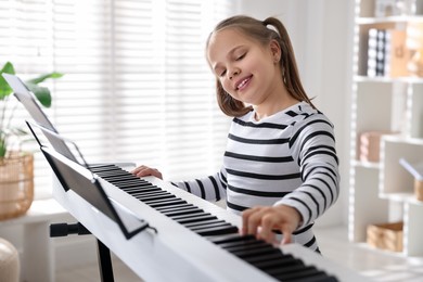 Photo of Cute girl playing synthesizer at home. Electronic musical instrument