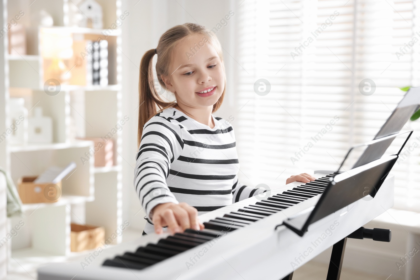 Photo of Cute girl playing synthesizer at home. Electronic musical instrument